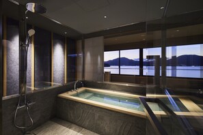 Un baño moderno con un jacuzzi con recinto de vidrio, ducha y vistas a un lago y montañas.