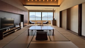 A modern living room with a large flat-screen TV, a dining table, two chairs, and a view of the sea through large windows. - Itsukushima Iroha  (Hatsukaichi)