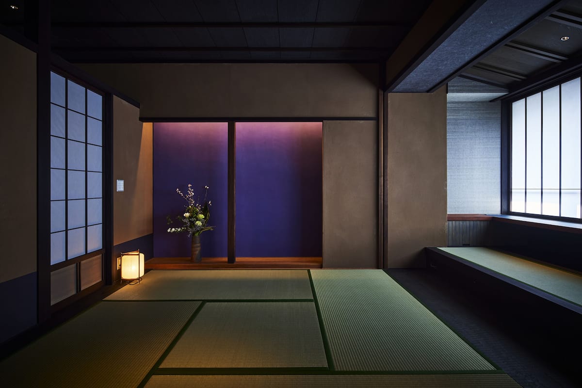 A traditional Japanese room with tatami flooring, sliding doors, and a small table with a vase of flowers.