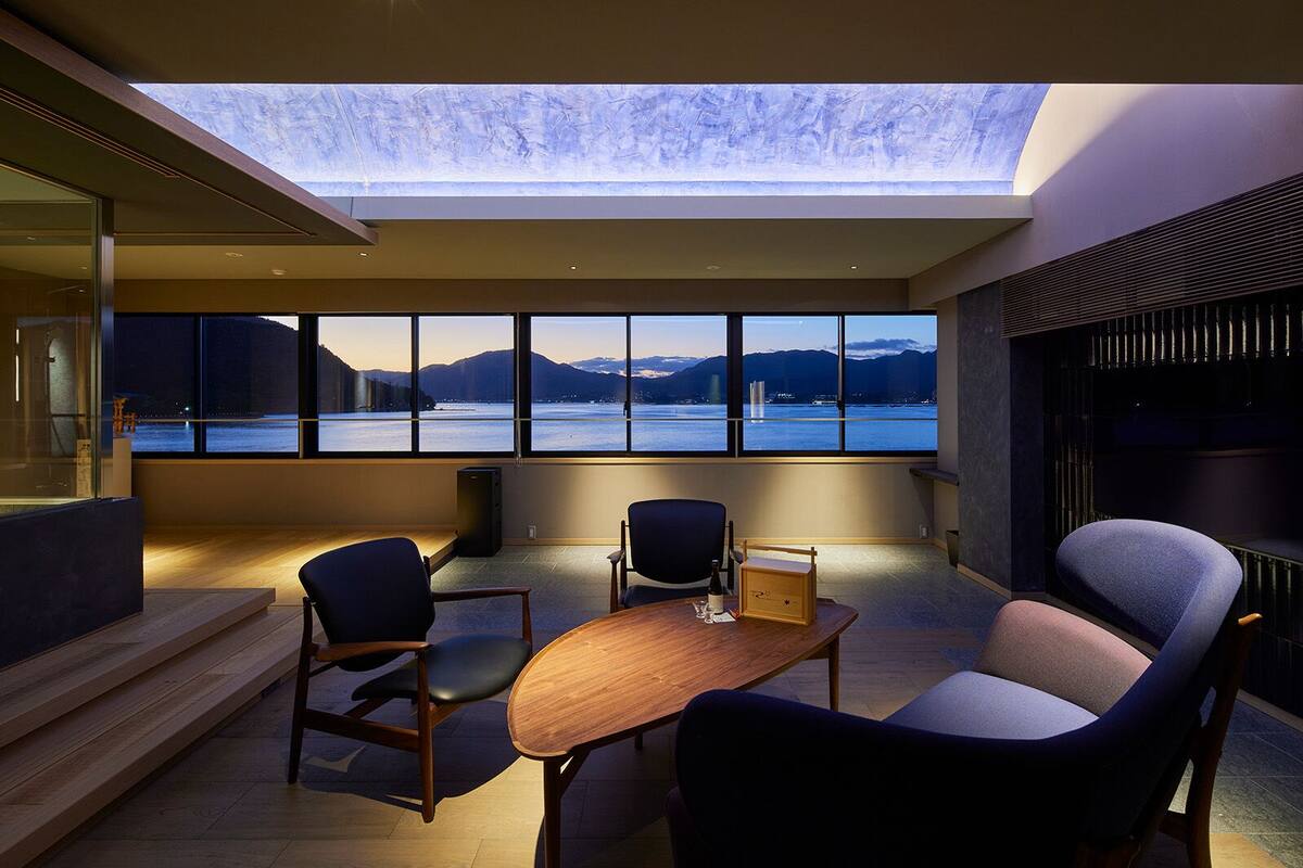 A modern interior with a skylight, large windows, and a view of a body of water and mountains.