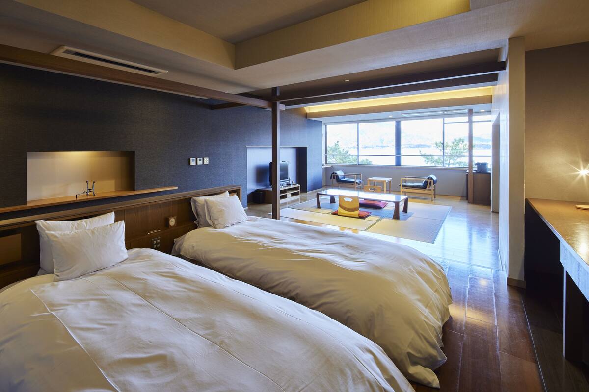 A modern hotel room with two large beds, a TV, a desk, and a view of the outdoors.