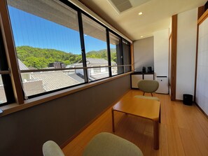 A modern room with a large window, a wooden table, two chairs, and a small kitchenette area.