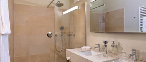 Un baño moderno con ducha de vidrio, dos lavamanos y un espejo grande.