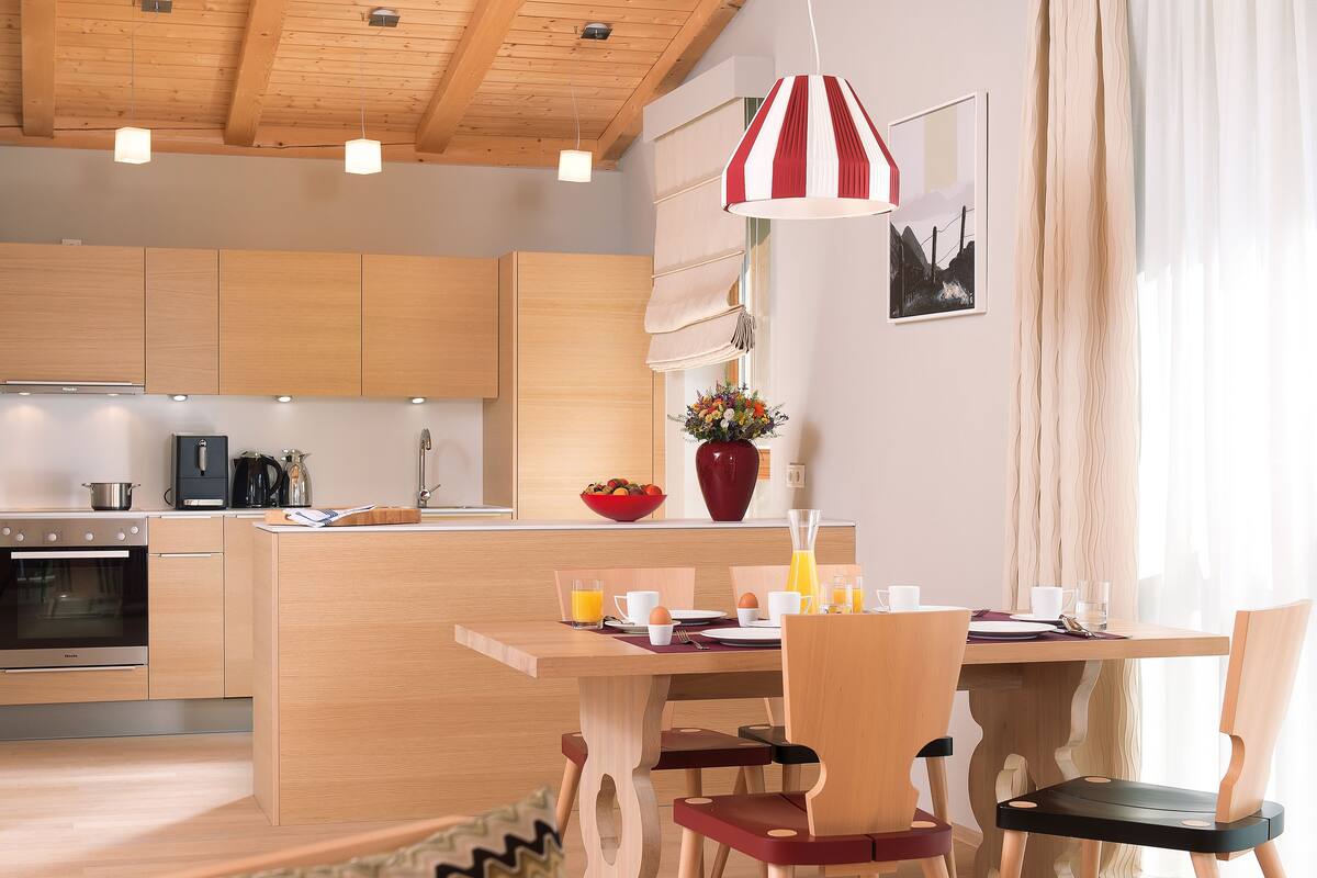 Eine moderne Küche mit Holzausstattung, einem Essbereich mit Holztisch und Stühlen sowie einer rot-weiß gestreiften Pendelleuchte.
