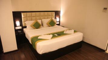 A neatly made bed with a tufted headboard, white linens, and green accent pillows. There are two bedside lamps on either side of the bed.