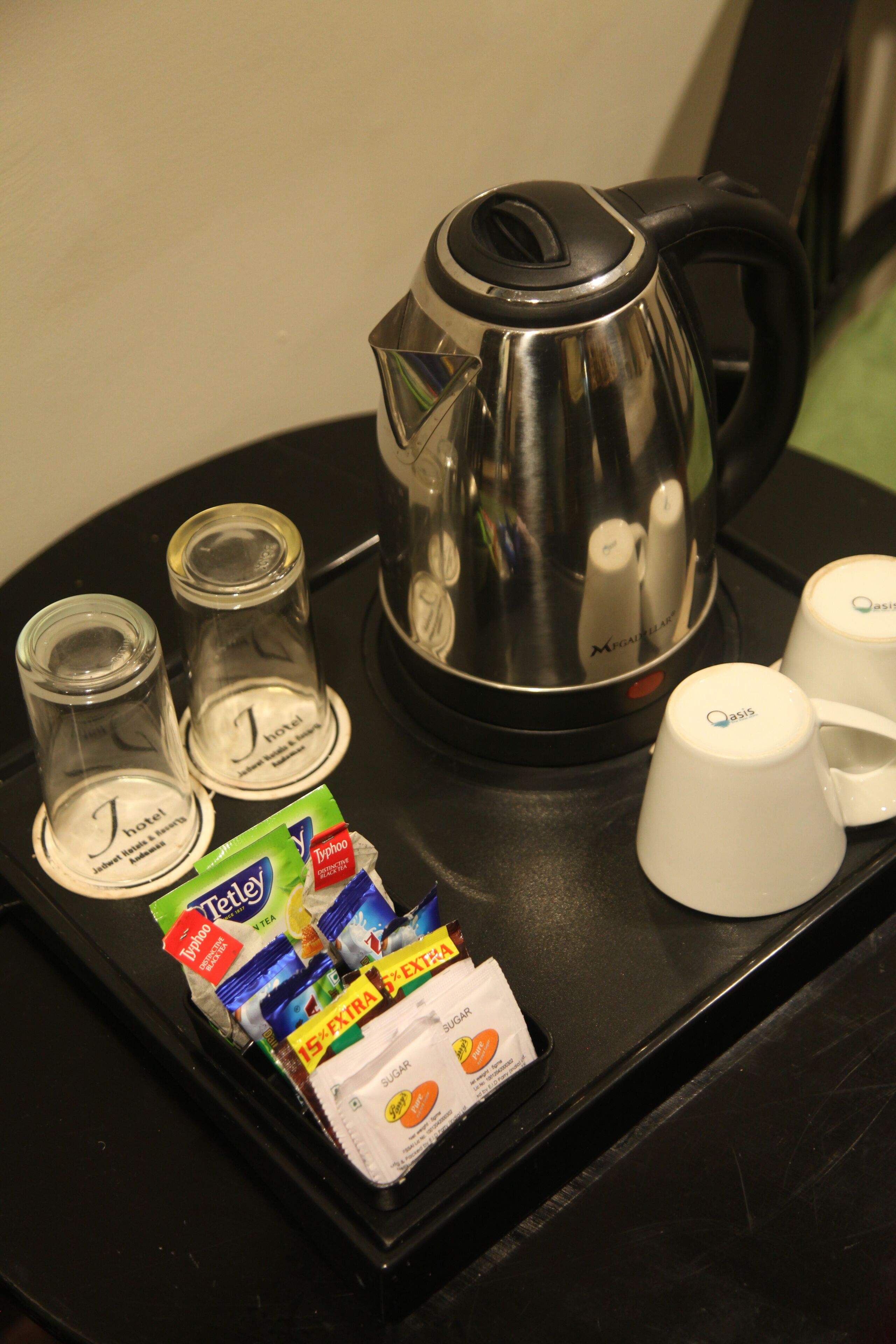 A tray with a coffee maker, two glasses, two cups, and packets of sugar and creamer.