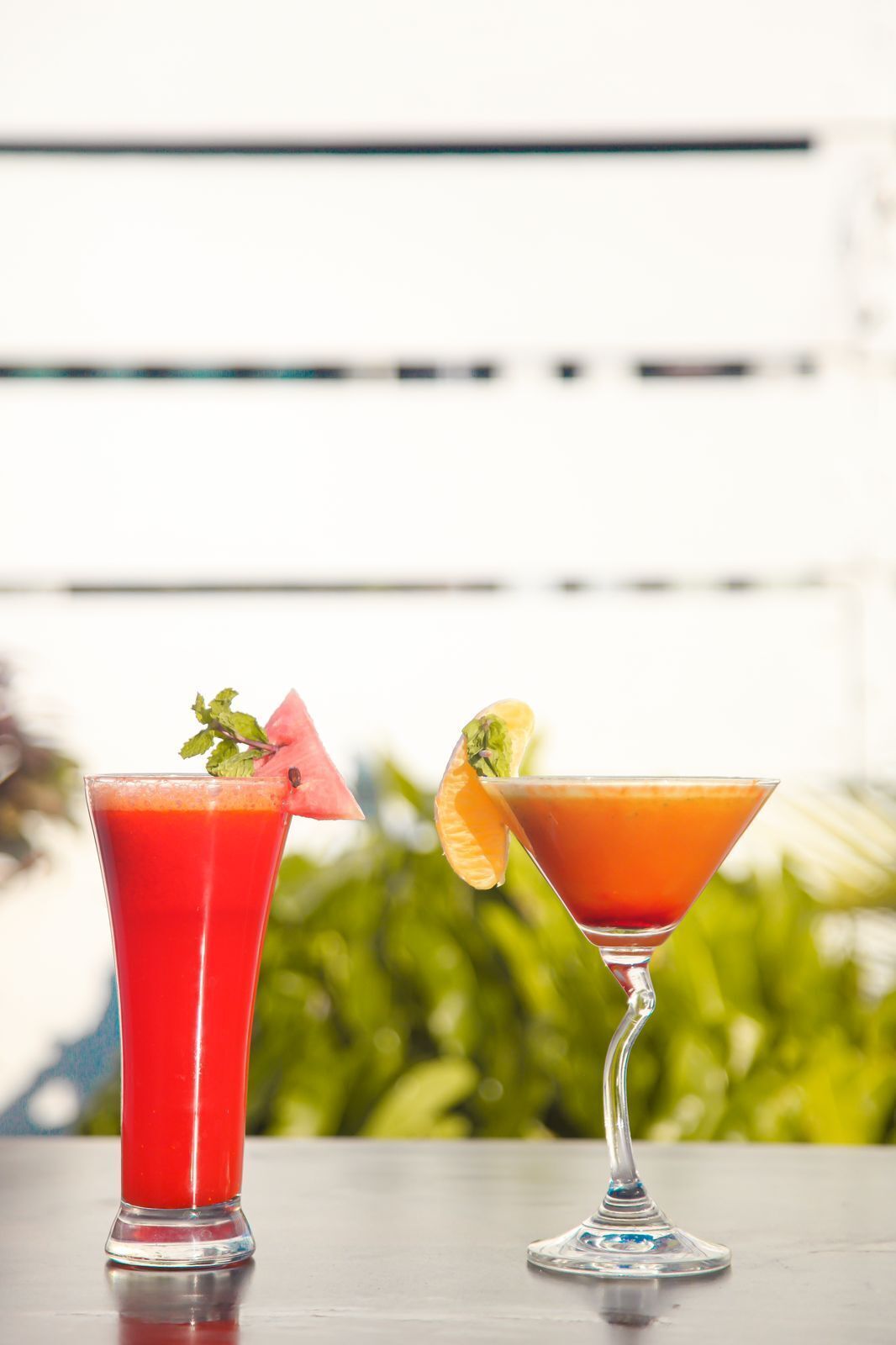 Two cocktails in martini glasses on a table with a blurred green background.