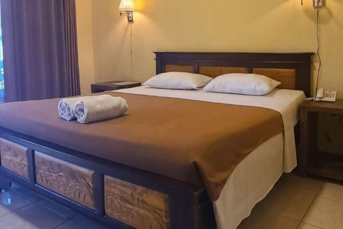 A neatly made bed with a brown bedspread, two pillows, and a rolled towel on the side.
