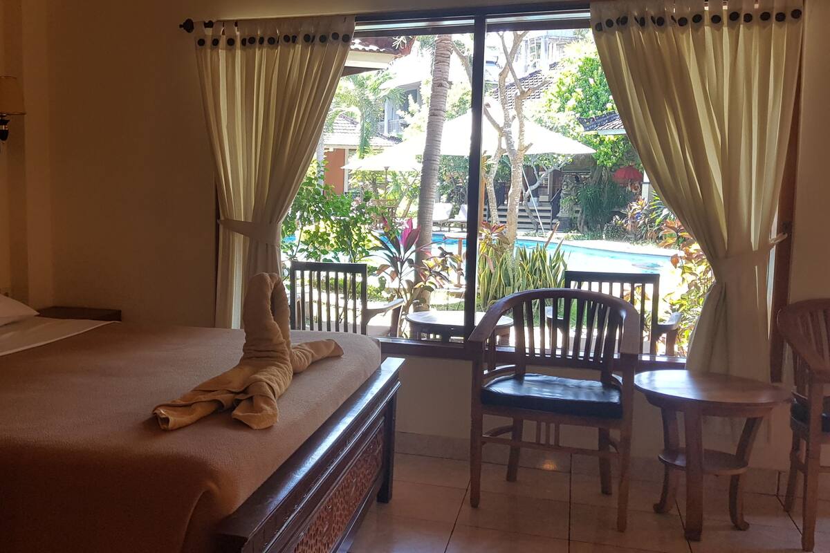 A hotel room with a bed, a small table, and chairs near a window with curtains.