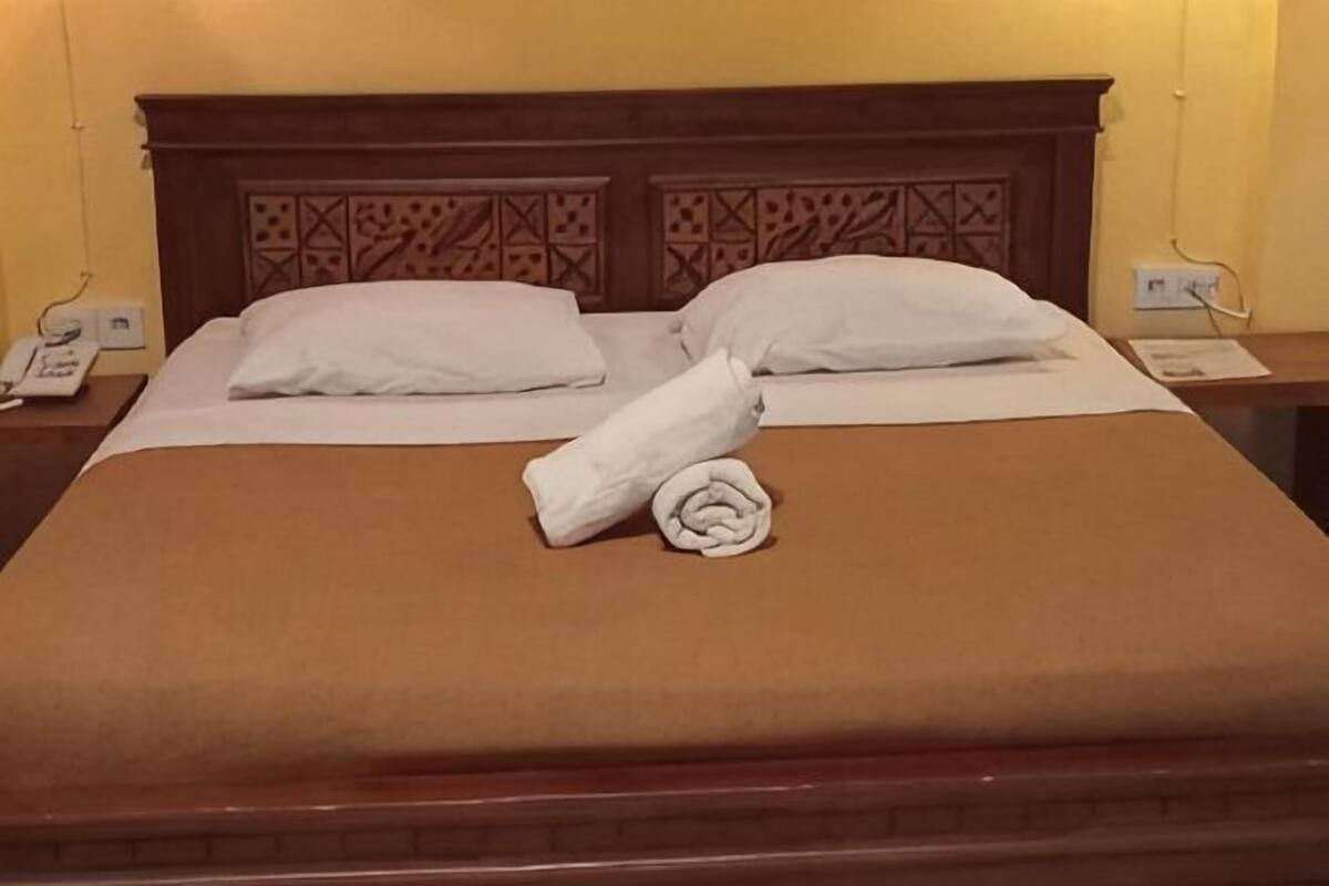 A neatly made bed with a brown bedspread, two white pillows, and a rolled towel.