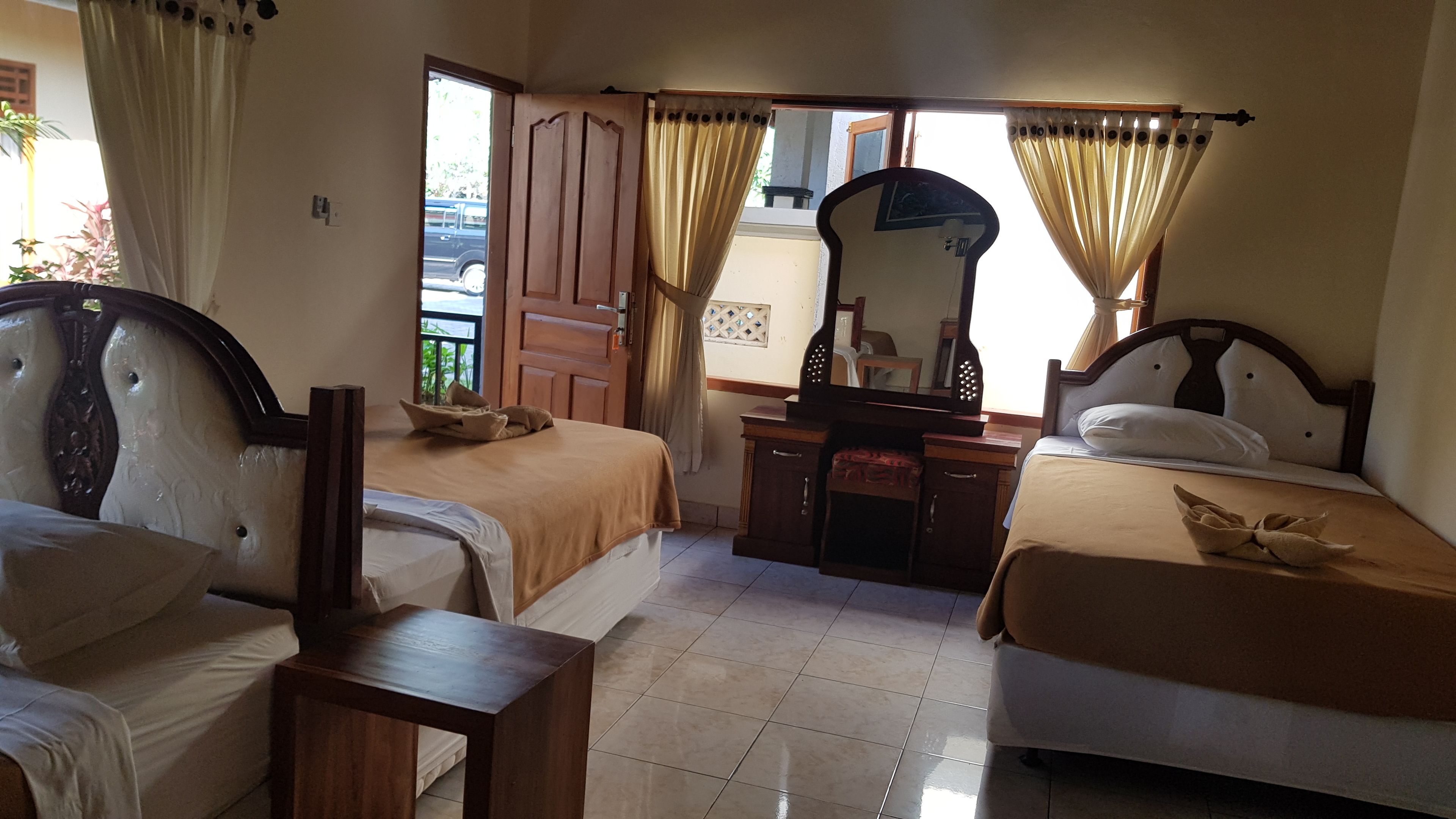 A hotel room with two beds, a wooden dresser, a mirror, and a window with curtains.