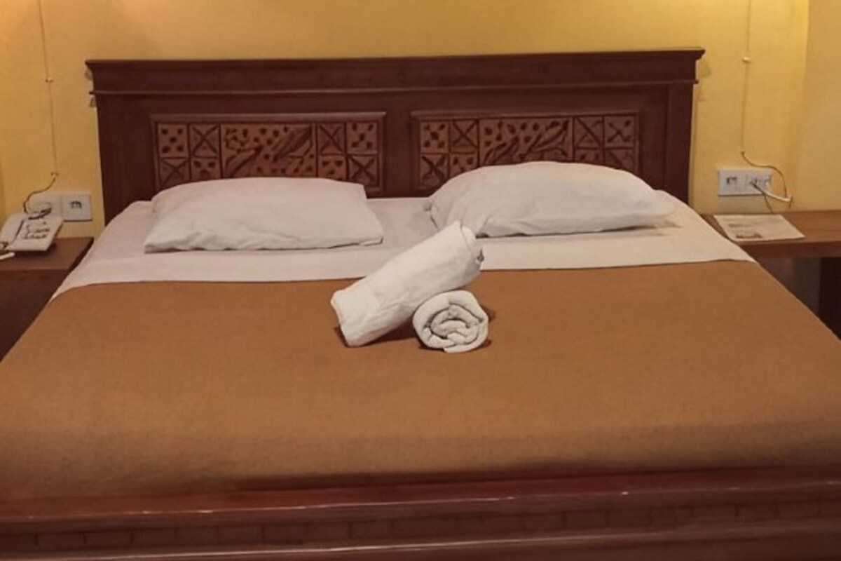 A neatly made bed with a brown bedspread, two white pillows, and a rolled towel.