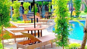 An outdoor pool area with lounge chairs and umbrellas, surrounded by lush greenery and a stone pathway. - Hotel Mylovina (Buleleng)