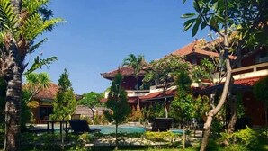 A resort with a pool, palm trees, and traditional architecture. - Hotel Mylovina (Buleleng)
