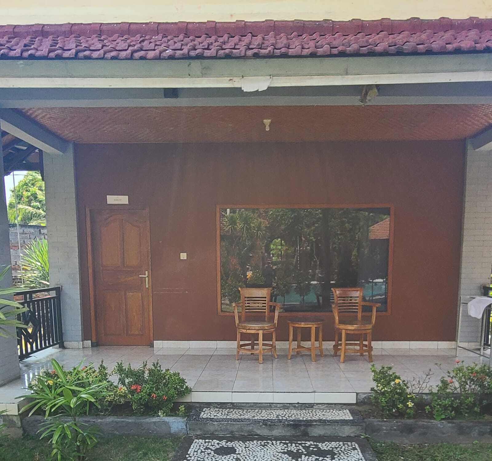 A covered outdoor seating area with a wooden door, a large window, and a tiled floor.