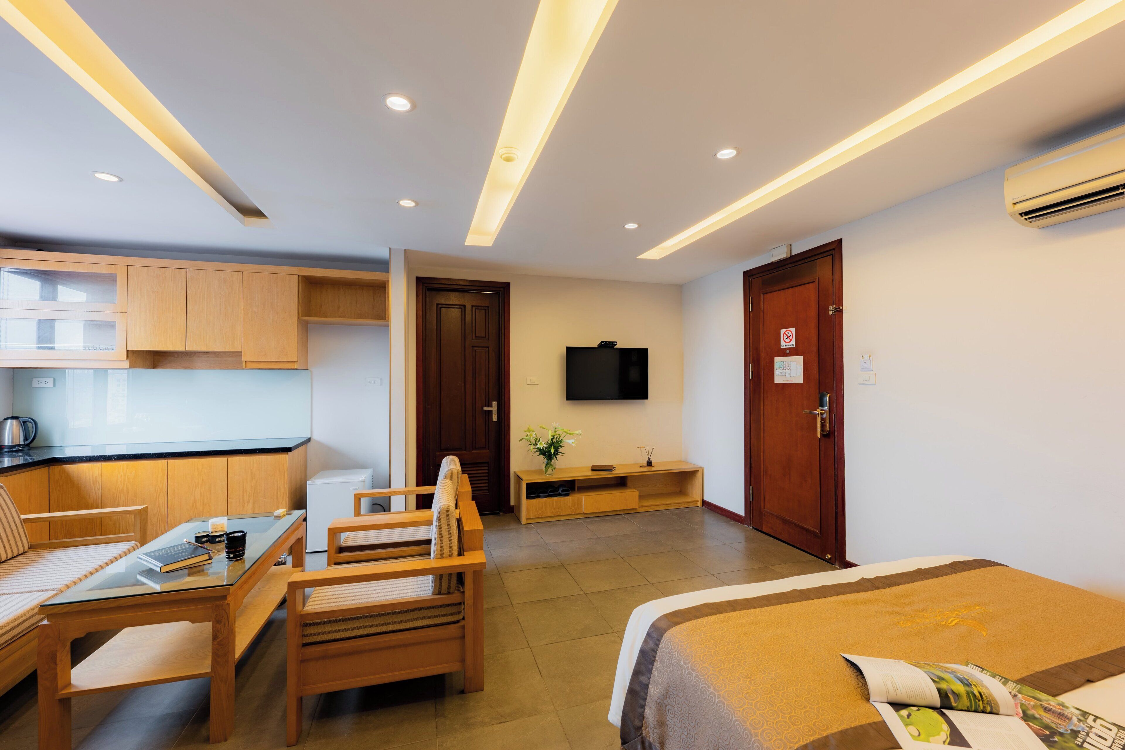 Quarto de hotel com uma cama, uma mesa com cadeiras, uma cozinha compacta e uma televisão na parede.