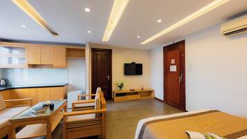 Quarto de hotel com uma cama, uma mesa com cadeiras, uma cozinha compacta e uma televisão na parede.