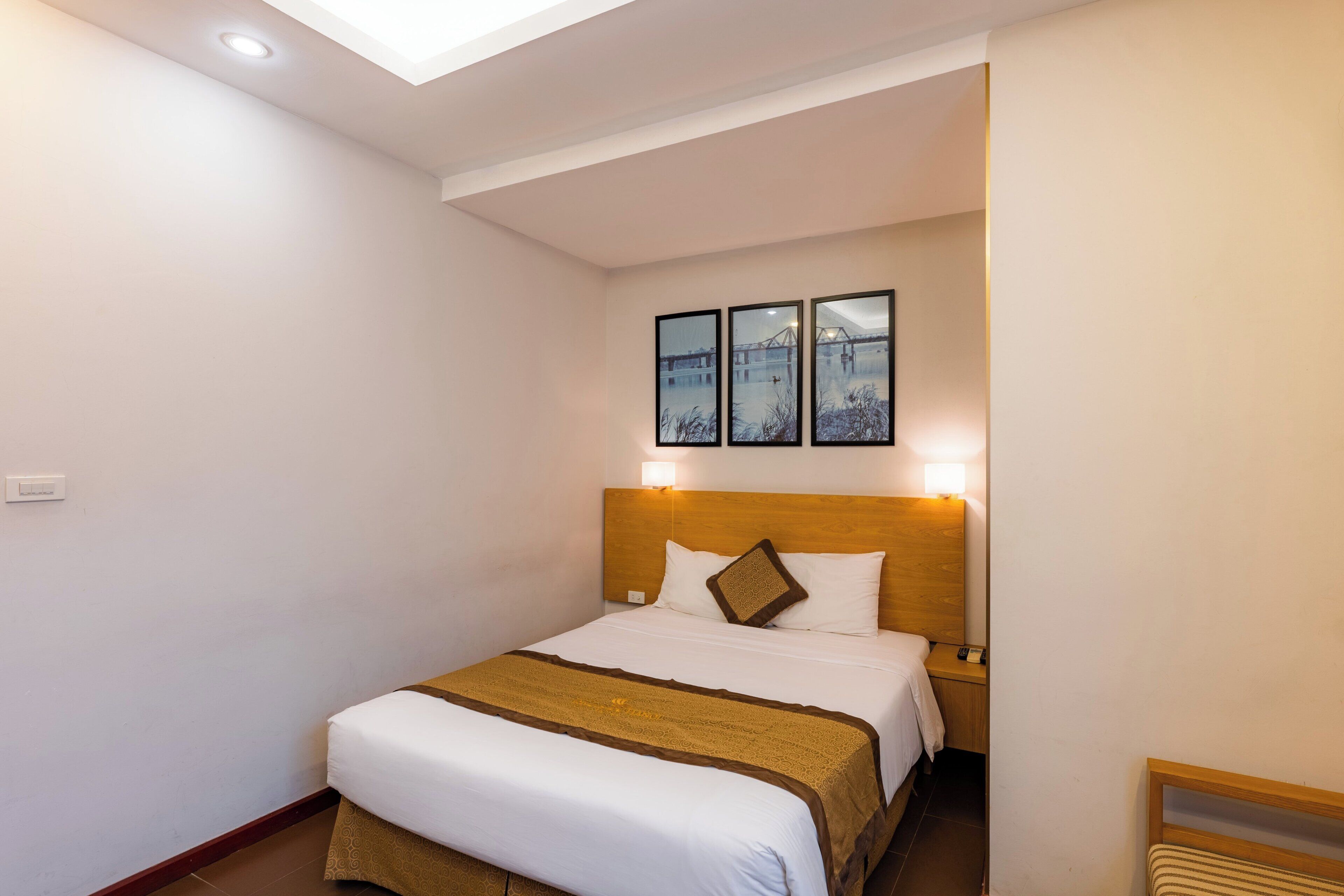 A hotel room with a bed, a nightstand, a wall-mounted light, and a ceiling light.