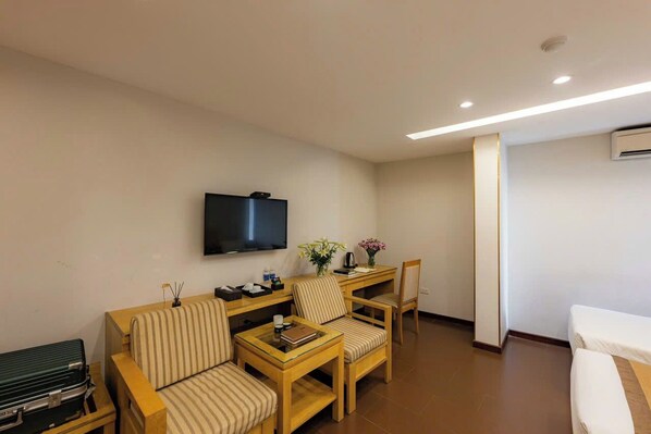 Una habitación de hotel con un sofá, dos sillones, una mesita, un televisor y una cama.