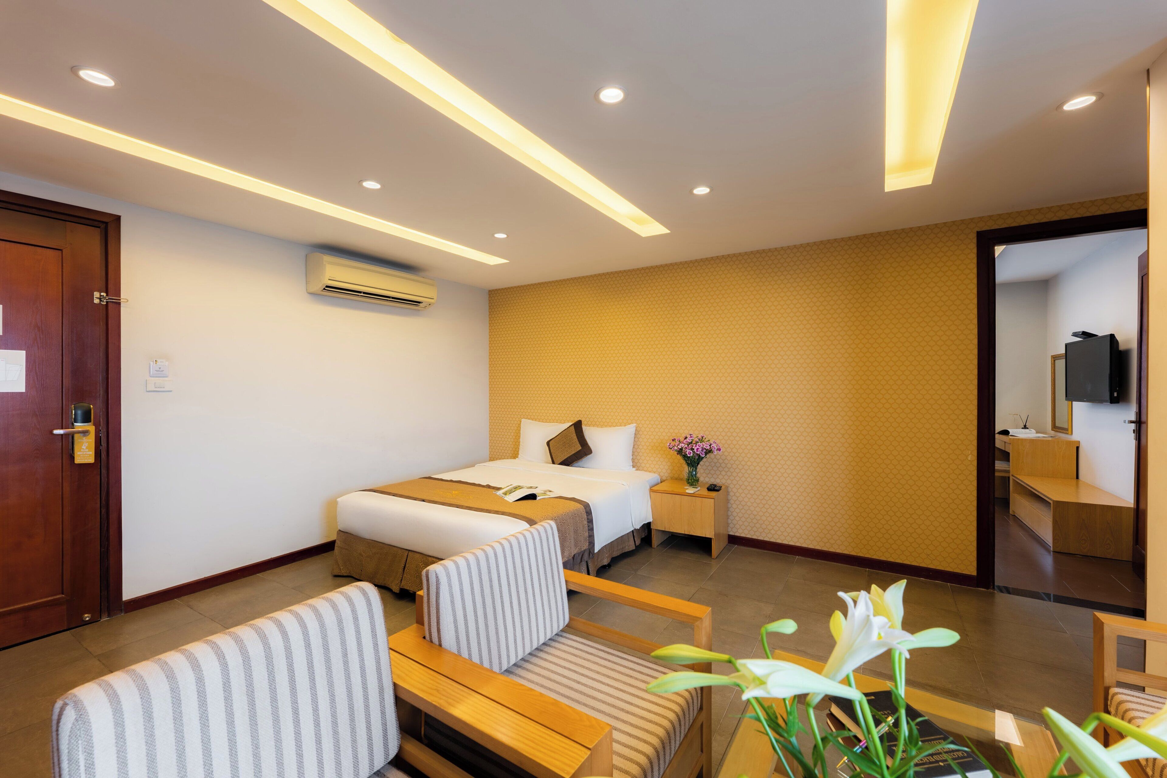 Habitación de hotel con cama, mesitas de noche, un espejo, un banco de madera y una planta en maceta.