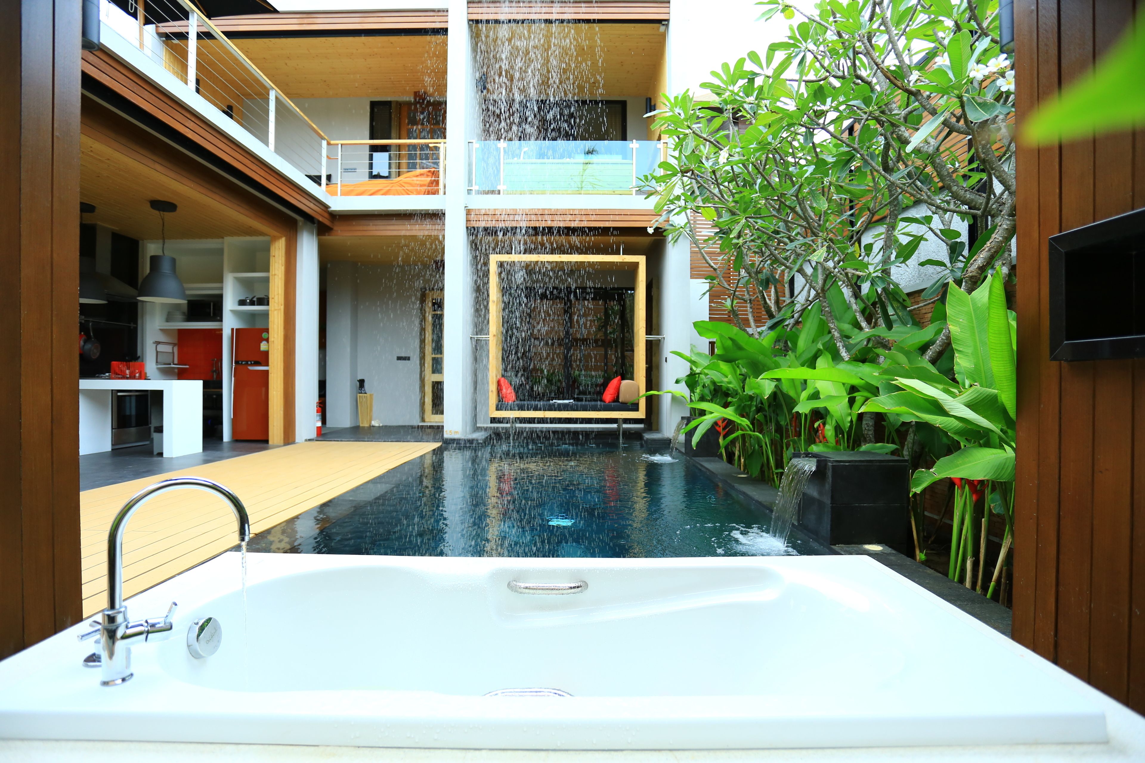 Piscina interior moderna con jacuzzi, rodeada de exuberante vegetación y una terraza de madera.