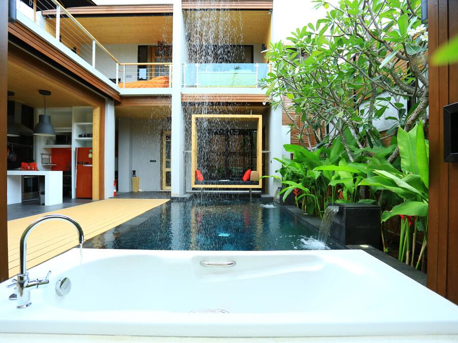 Piscina interior moderna con jacuzzi, rodeada de exuberante vegetación y una terraza de madera.