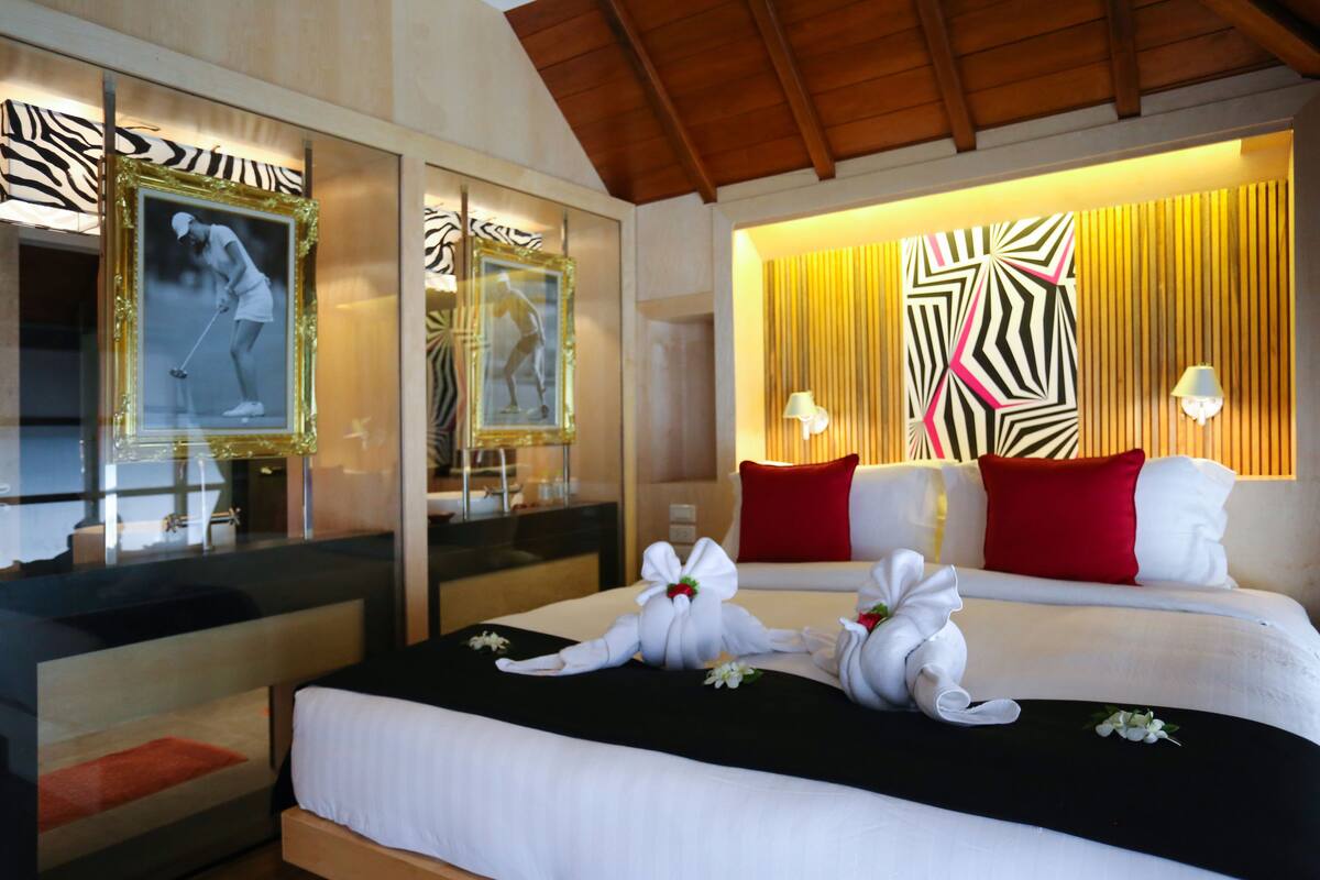 A hotel room with a bed, a mirror, a zebra-striped wall, and a red pillow.