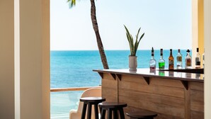 Zona bar con un bancone in legno, una pianta in vaso e bottiglie di liquore. Ci sono due sgabelli e vista sull'oceano.