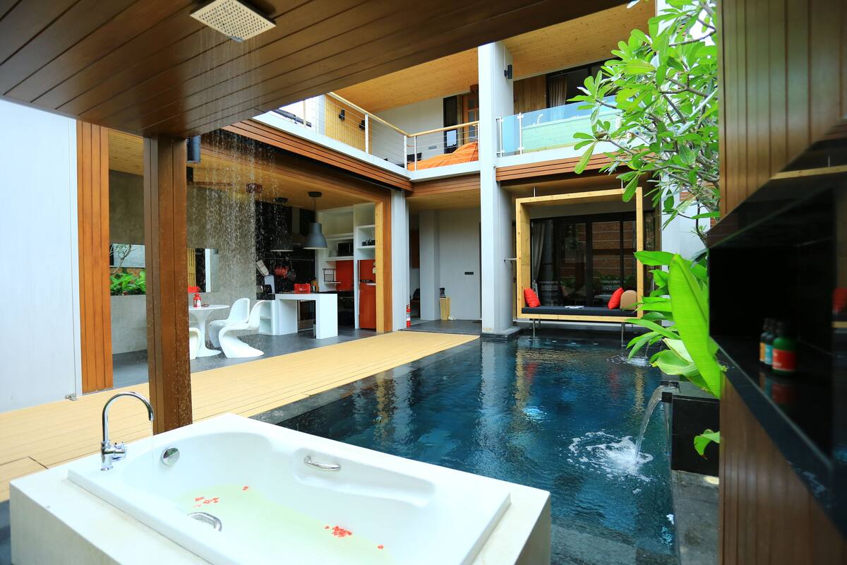 A modern indoor pool area with a jacuzzi, wooden deck, and a dining area with outdoor seating.