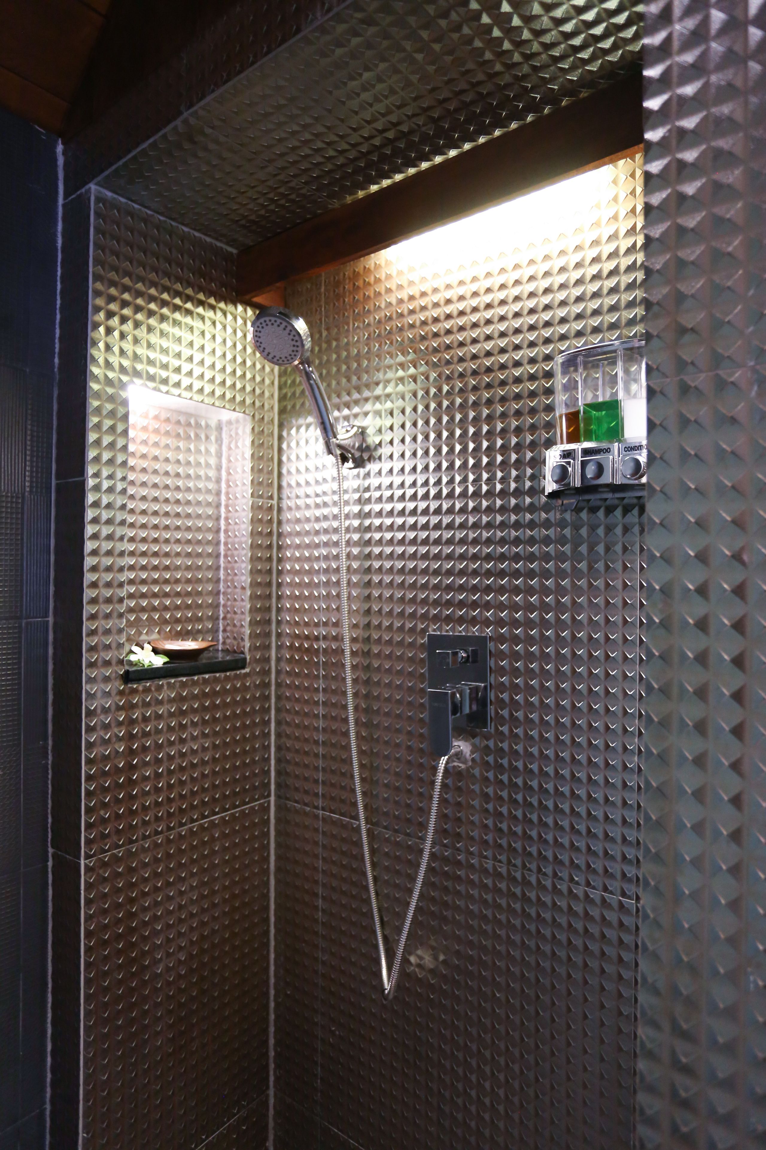 A shower with a handheld showerhead, a wall-mounted control panel, and a shelf with toiletries.