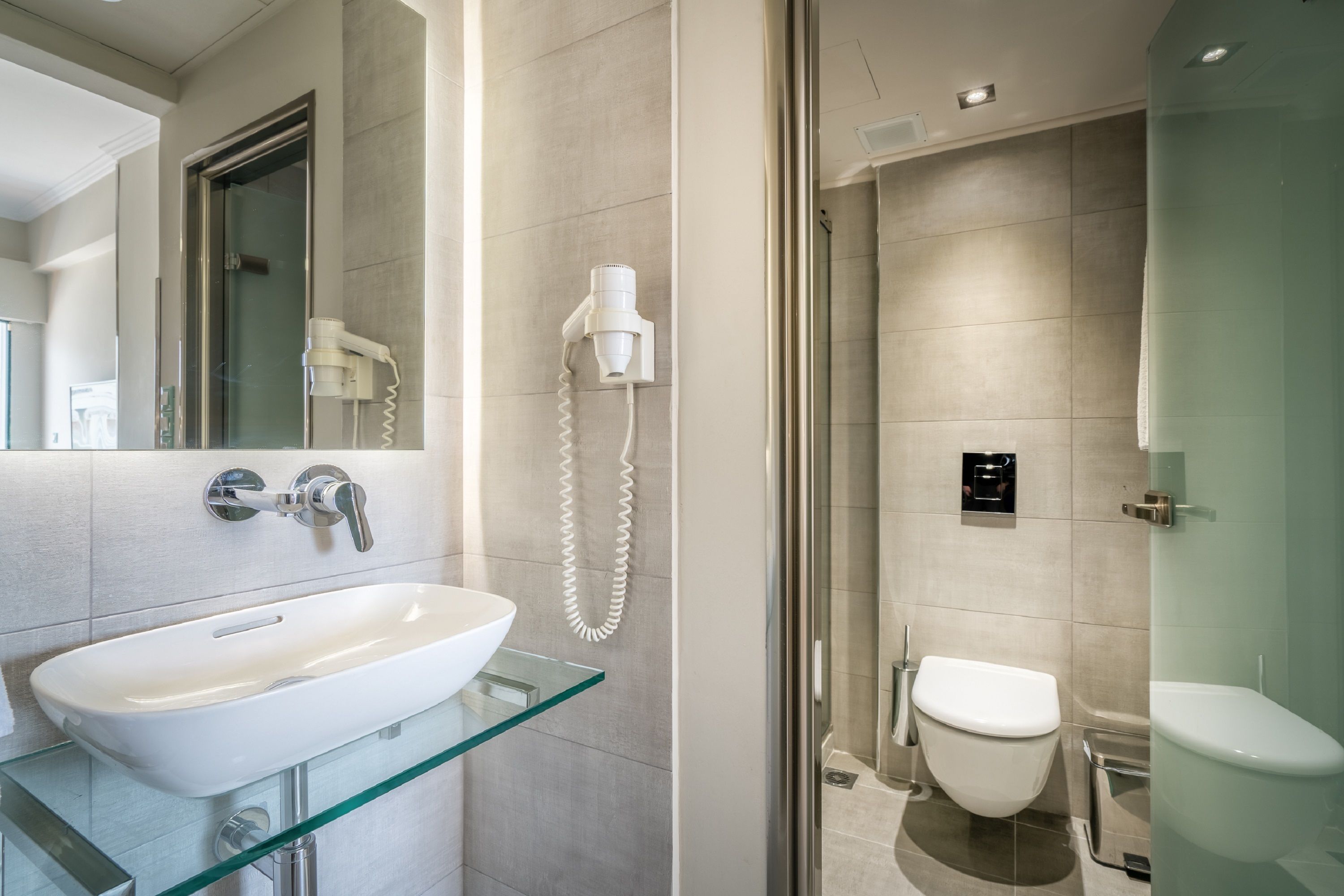 Une salle de bain moderne avec un lavabo en verre, un sèche-cheveux portatif et des toilettes.