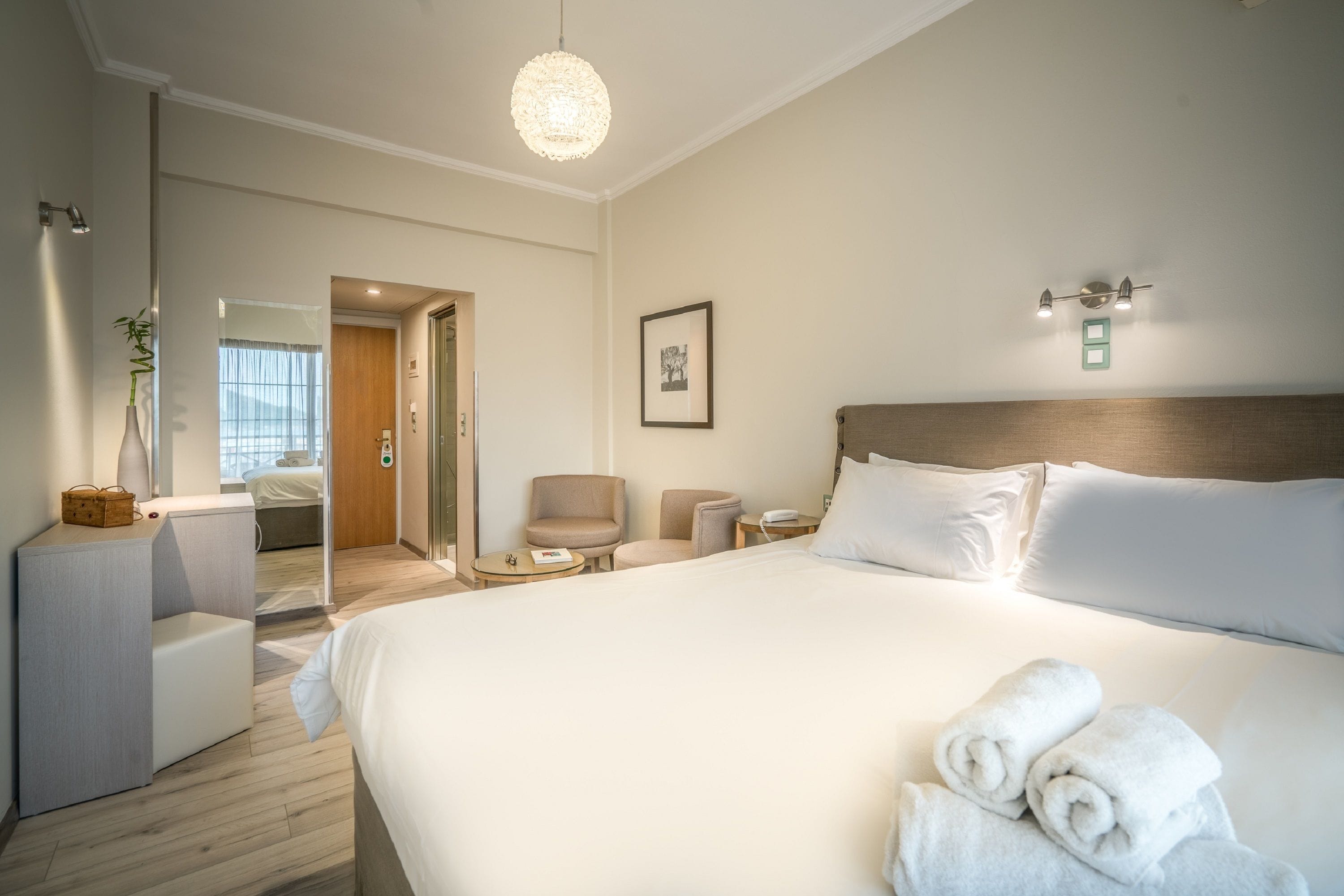 Ein Hotelzimmer mit einem großen Bett, Nachttischen, einem Sessel, einem kleinen Tisch, einem Spiegel und einer Pendelleuchte.