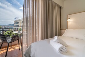 Habitación de hotel con cama, una silla, una mesa y vista al mar y edificios.
