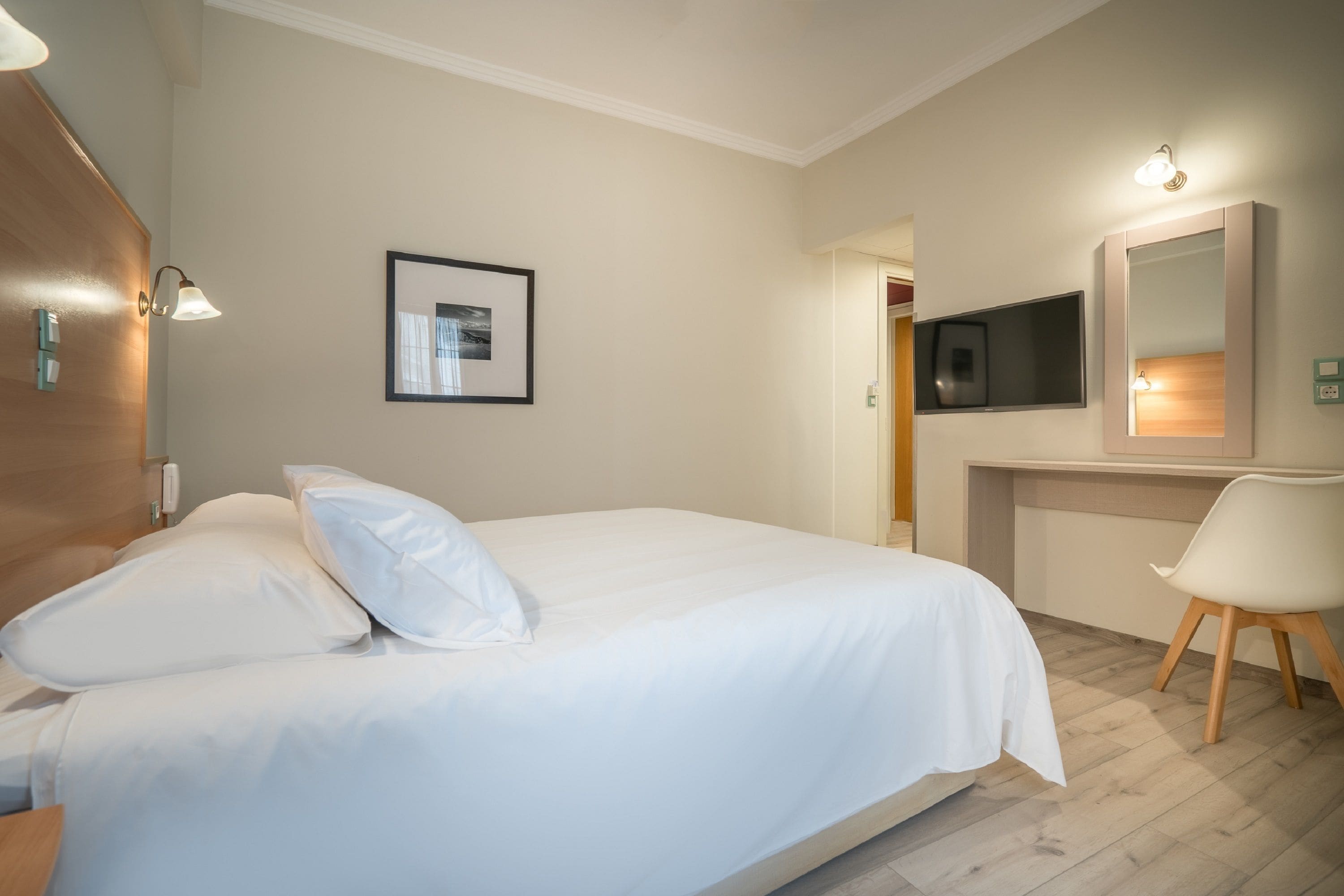 Quarto de hotel com cama, escrivaninha, cadeira, televisão e quadro na parede.