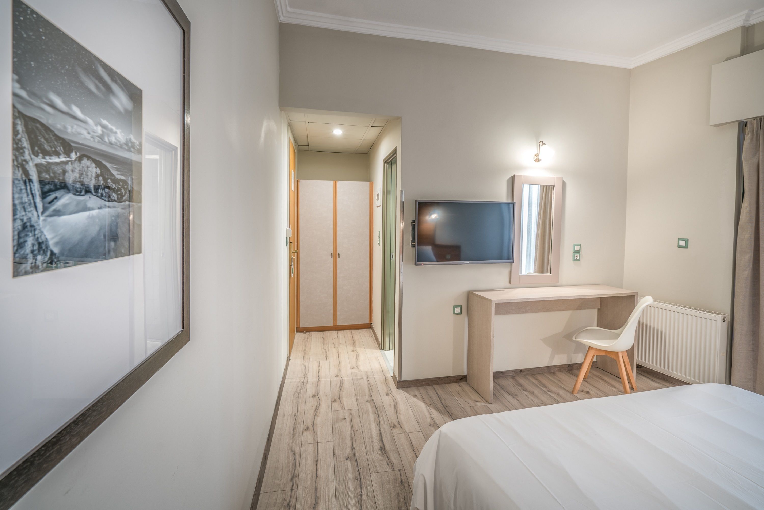 A hotel room with a bed, a desk with a chair, a TV, and a framed picture on the wall.