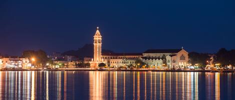 Vista panorámica del frente marítimo de una ciudad, con edificios iluminados y una torre destacada que se refleja en el agua.