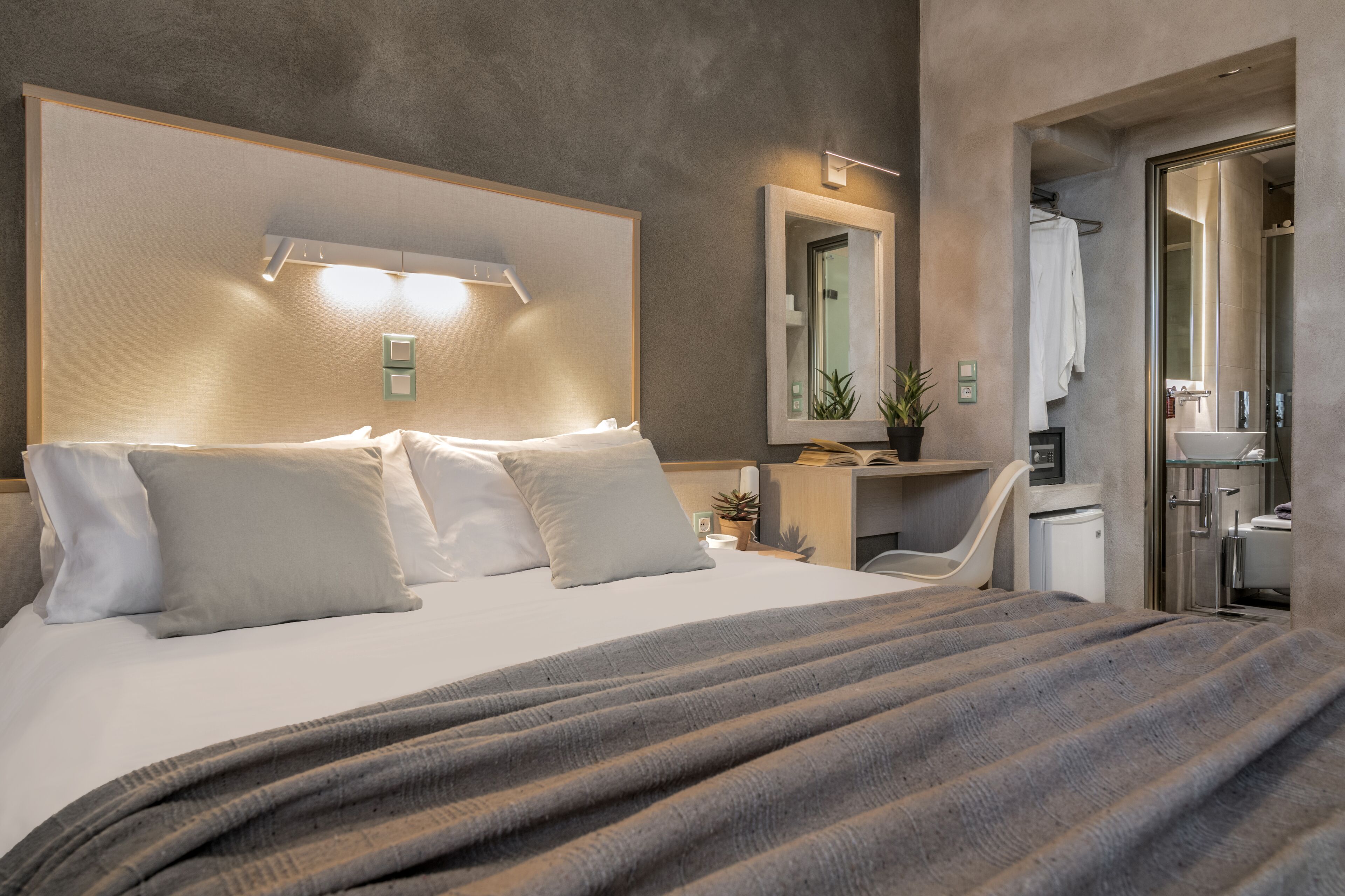 Quarto de hotel moderno com uma cama grande, mesa de cabeceira e banheiro visível por uma porta aberta.