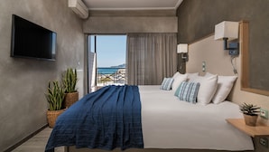 A hotel room with a bed, a TV, a potted plant, and a view of the city.