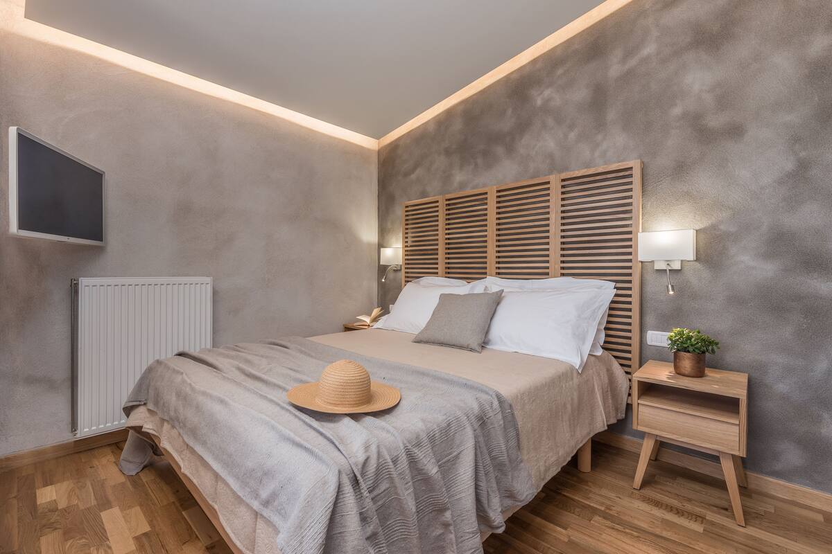 A modern bedroom with a large bed, a bedside table with a lamp, a radiator, and a TV mounted on the wall.