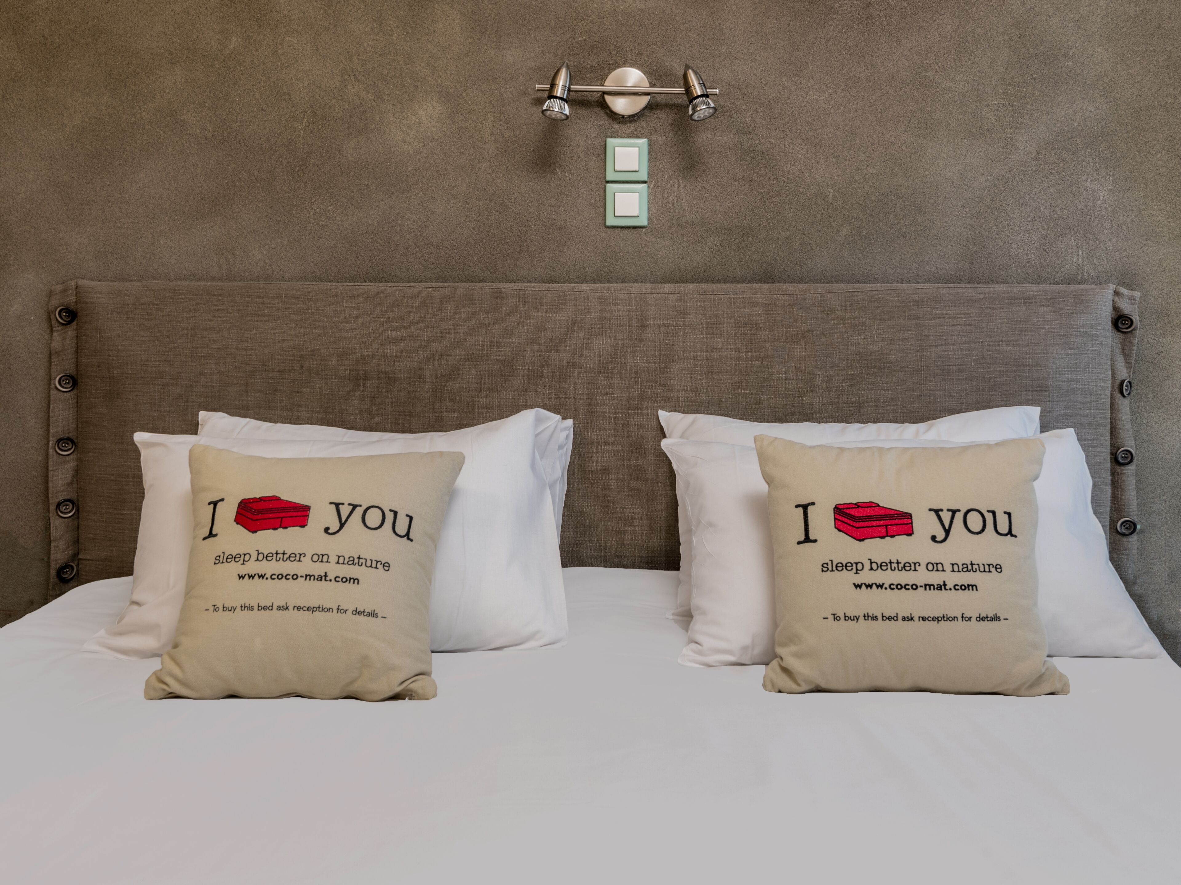 Una cama con dos almohadas, cada una con una maleta roja y el texto 'Duermo mejor en la naturaleza'.