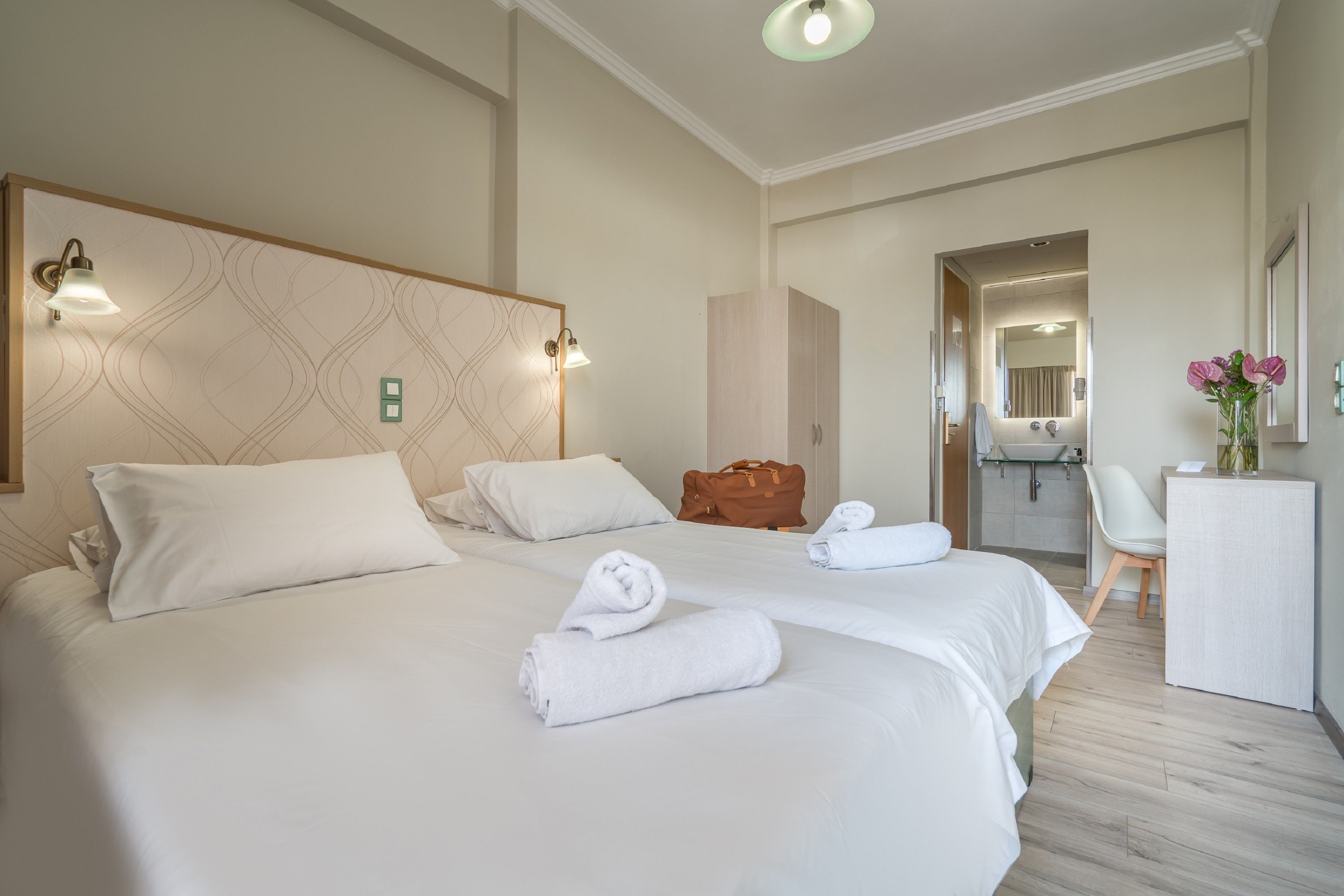 A hotel room with two beds, a desk, a chair, a bathroom, and a mirror.