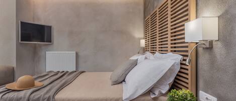 Ein Schlafzimmer mit einem Bett, einem an der Wand befestigten Fernseher, einem Holz-Kopfteil und einem Nachttisch mit einer Pflanze.