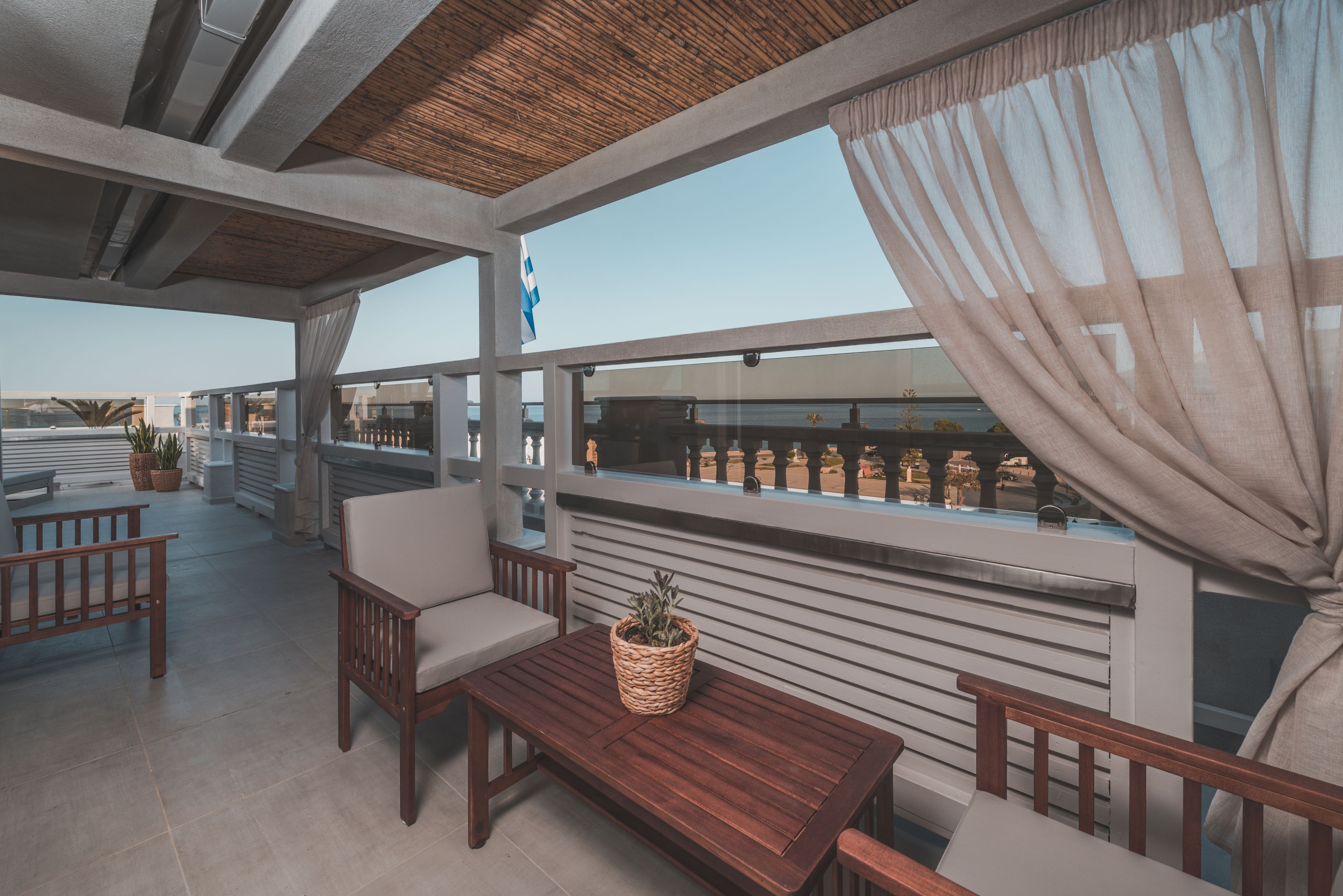 Un patio exterior con mobiliario de madera, una cesta tejida con una planta y vistas a la playa.