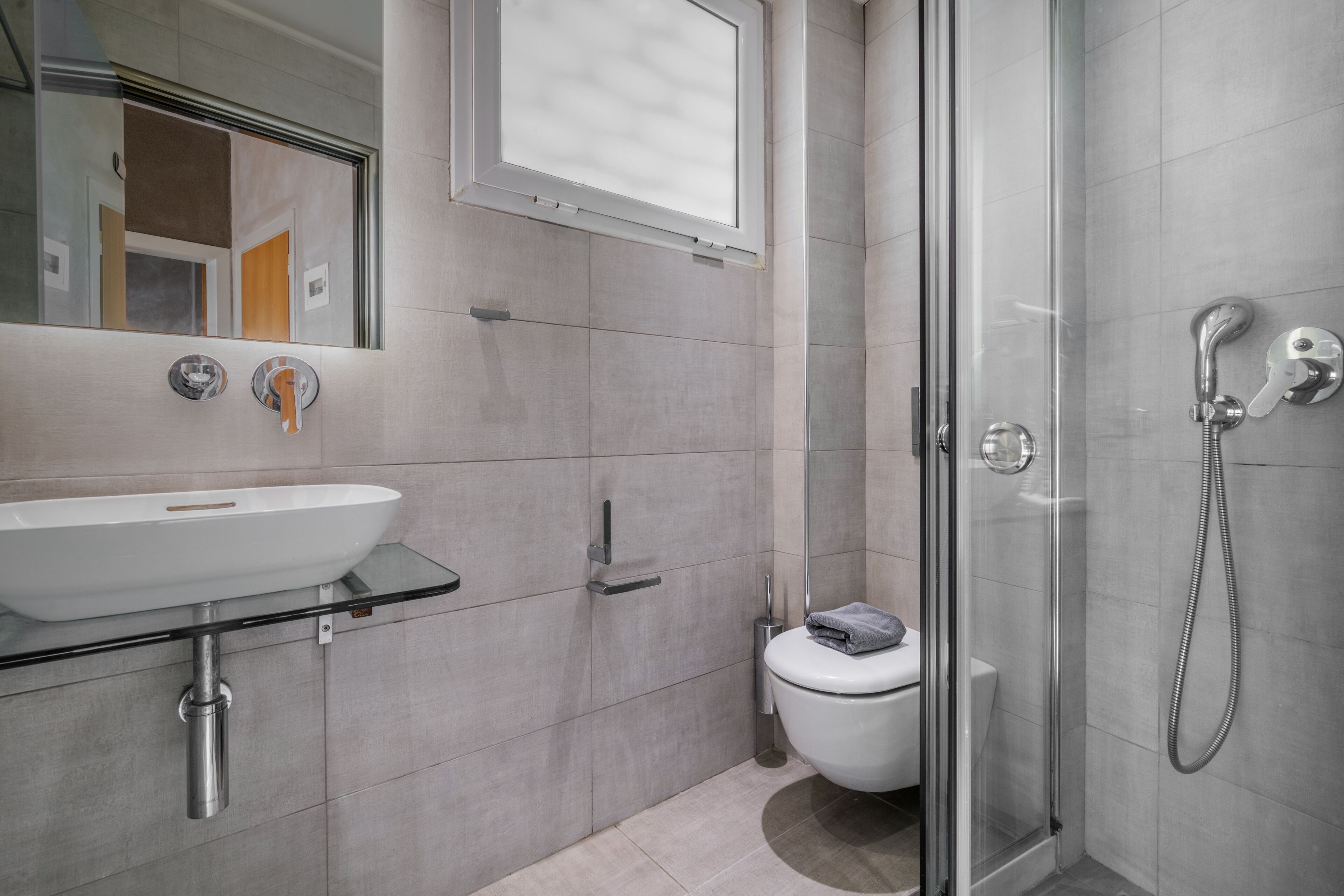 A modern bathroom with a glass sink, a toilet, and a shower.