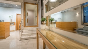 A modern reception area with a glass desk, wooden reception desk, and a staircase leading to an upper floor.