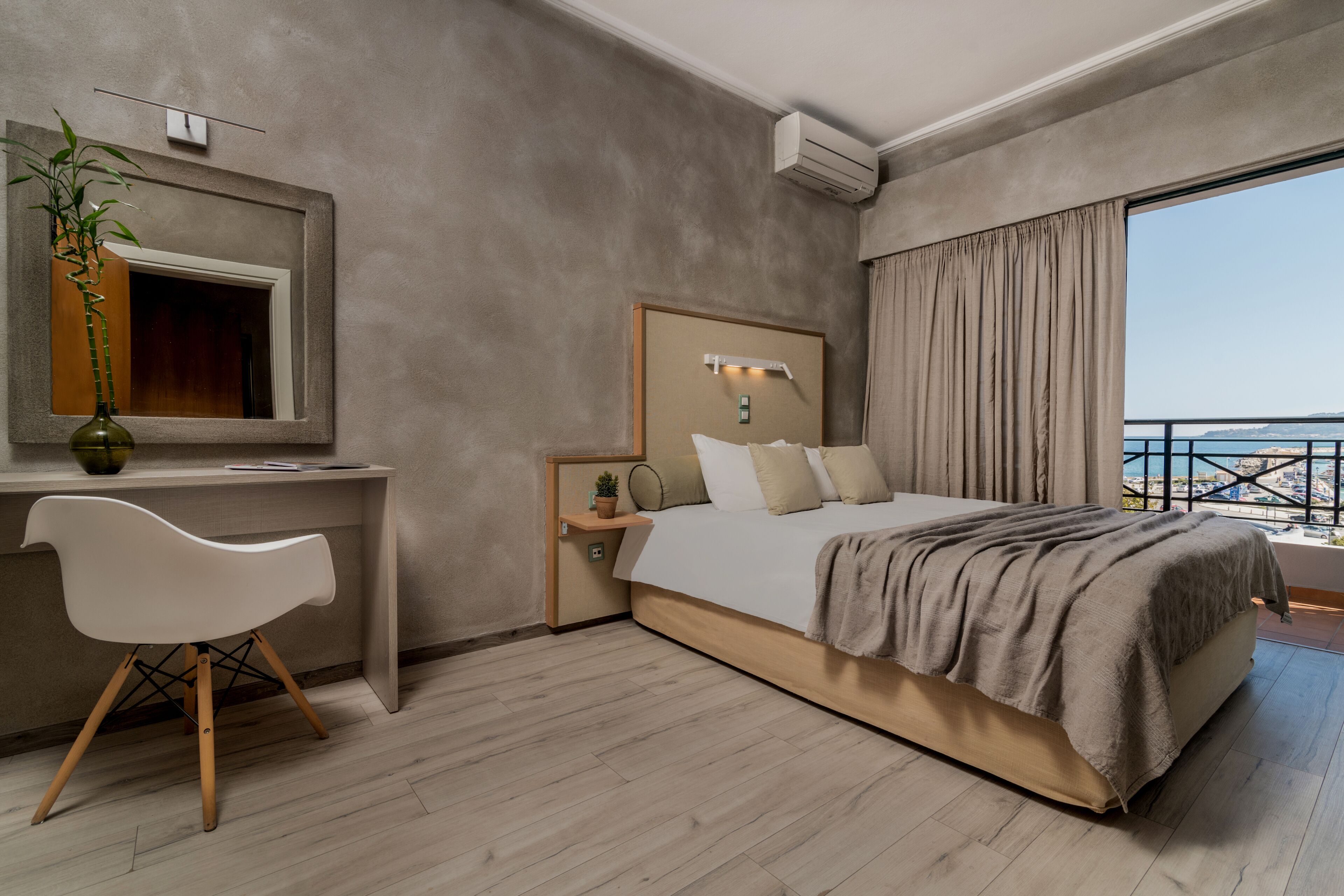 Una habitación de hotel moderna con cama, escritorio, silla y un amplio ventanal con vistas.