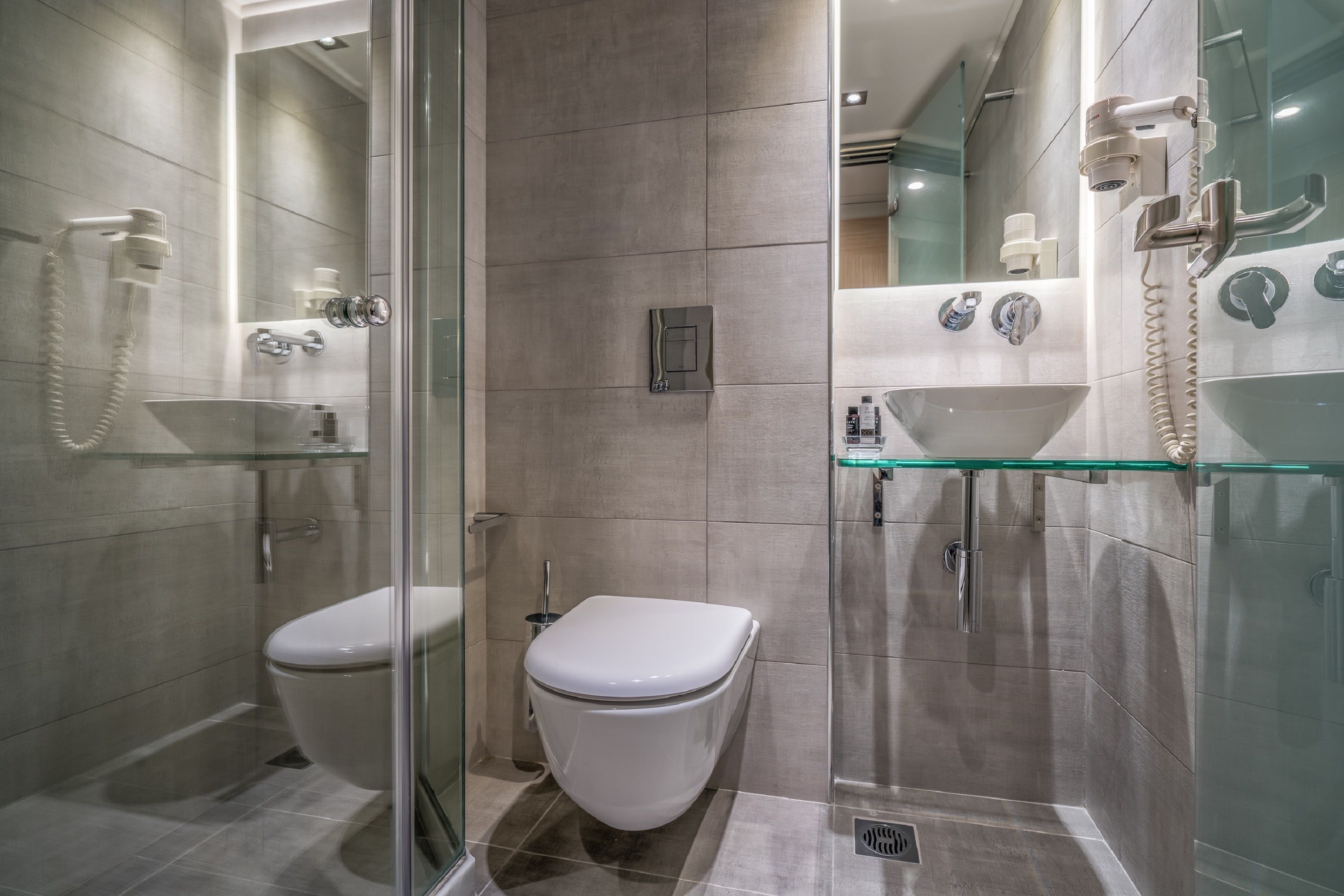A modern bathroom with a glass shower enclosure, a white toilet, and a glass sink with a mirror above it.