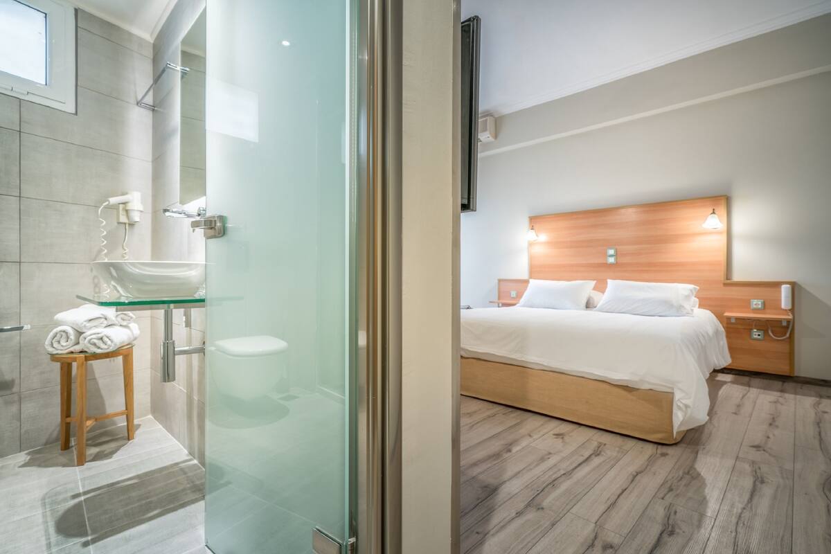 A modern bathroom with a glass shower enclosure, a wooden stool with towels, and a white sink.