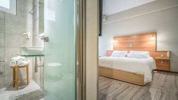 Ein modernes Badezimmer mit Duschkabine aus Glas, einem Holzschemel mit Handtüchern und einem weißen Waschbecken.