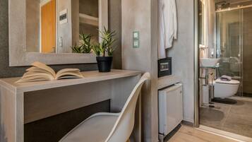 A modern bathroom with a built-in desk, a potted plant, a towel rack, and a glass shower enclosure.